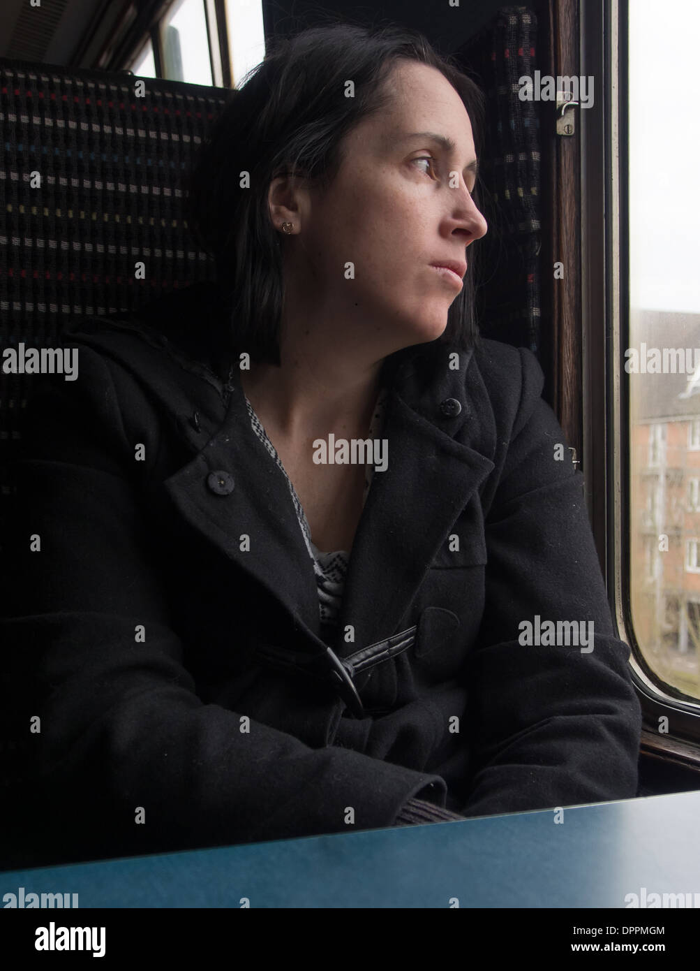 A bored lady sits looking out of a train window. Stock Photo
