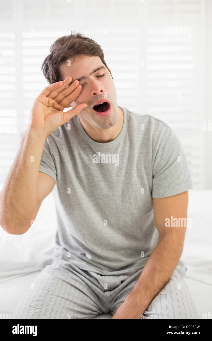Sleepy man yawning as he rubs his eye in bed Stock Photo