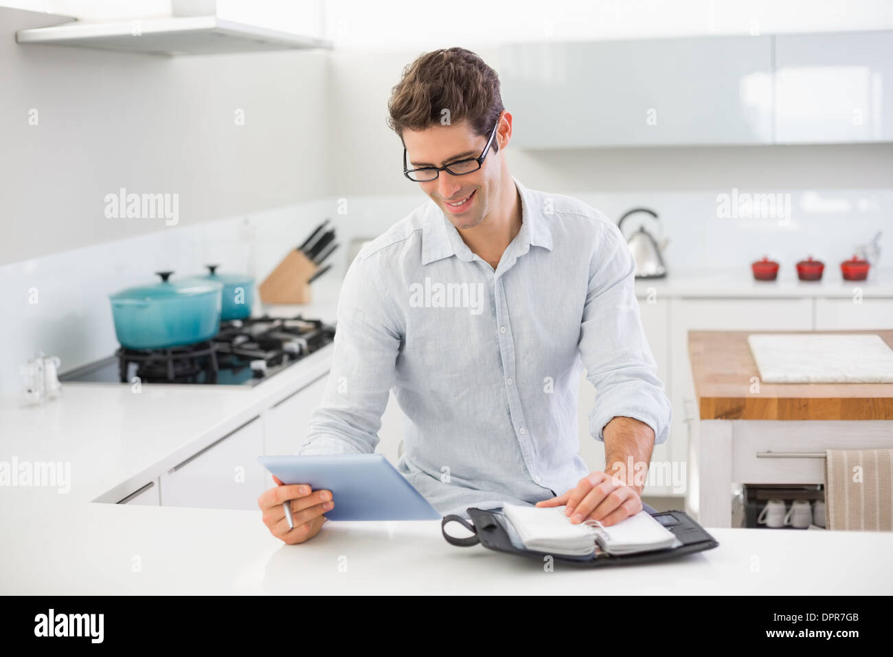 Casual man with digital tablet and diary in kitchen Stock Photo
