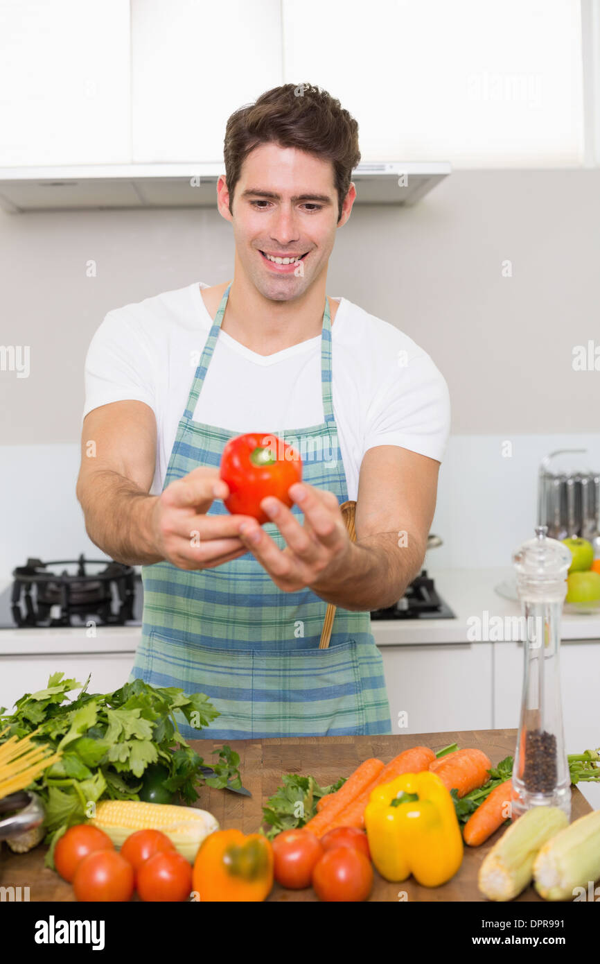 Smiling man holding out bell pepper with vegetables in kitchen Stock Photo