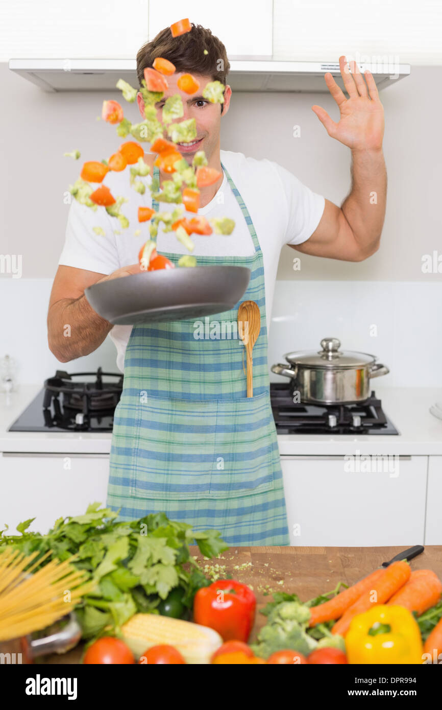 Cheerful man tossing vegetables in kitchen Stock Photo