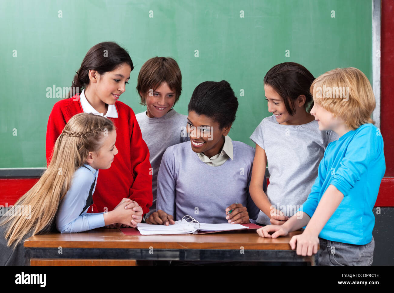 Happy Teacher Teaching Schoolchildren At Desk In Classroom Stock Photo