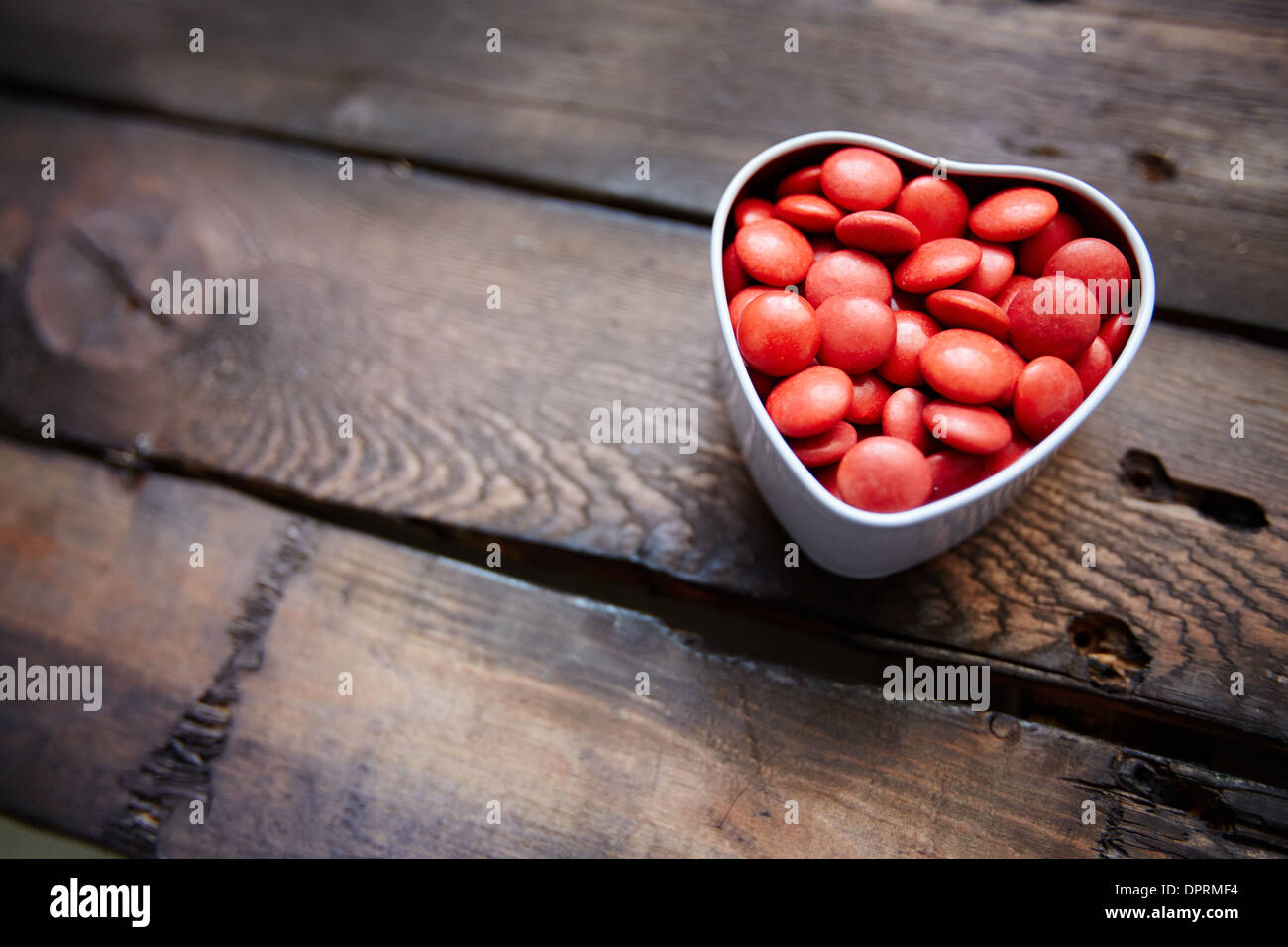 Red small candies in heart shaped box against wooden background Stock Photo