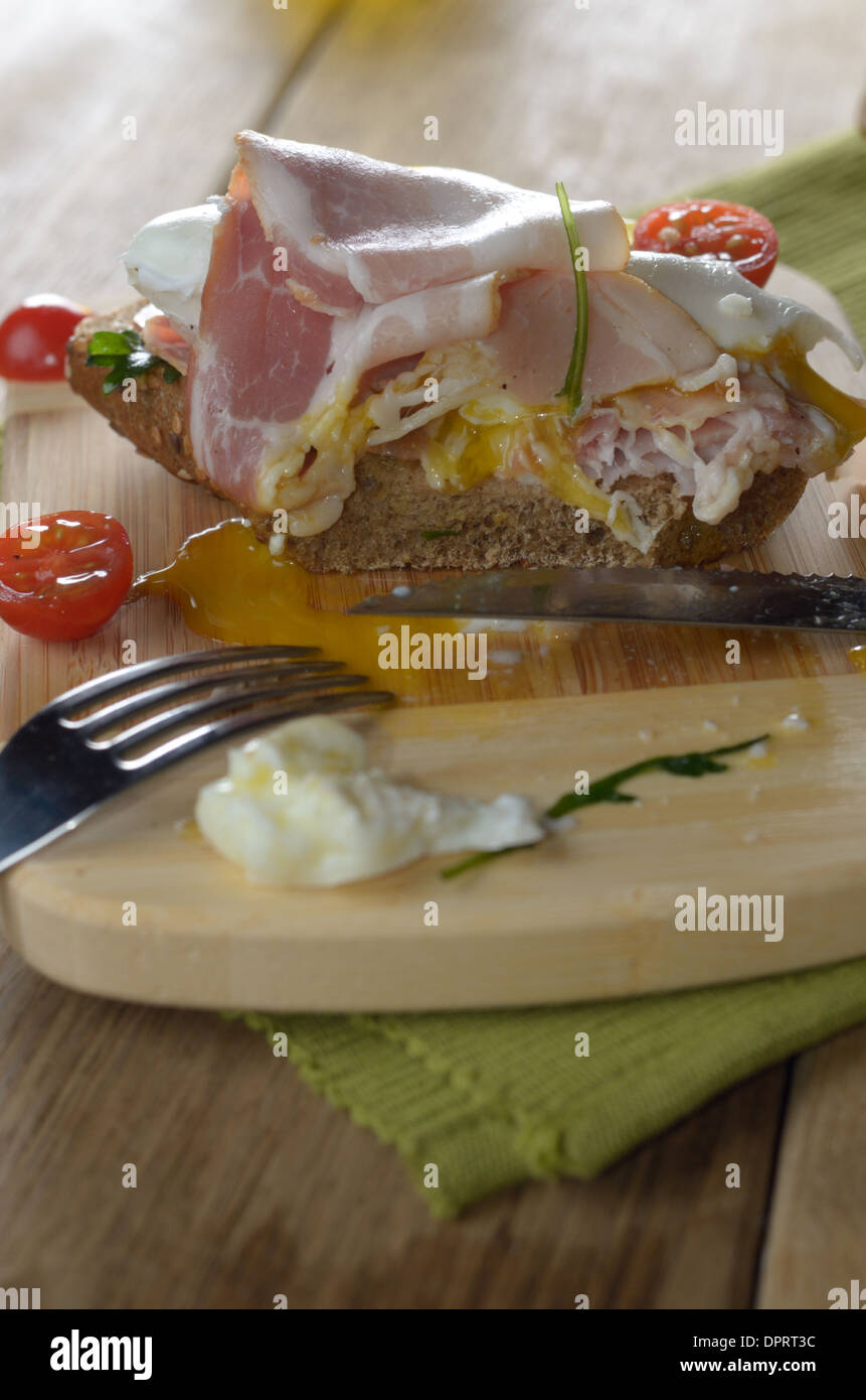 Unfinished bacon and poached eggs open sandwich on the cut board Stock Photo