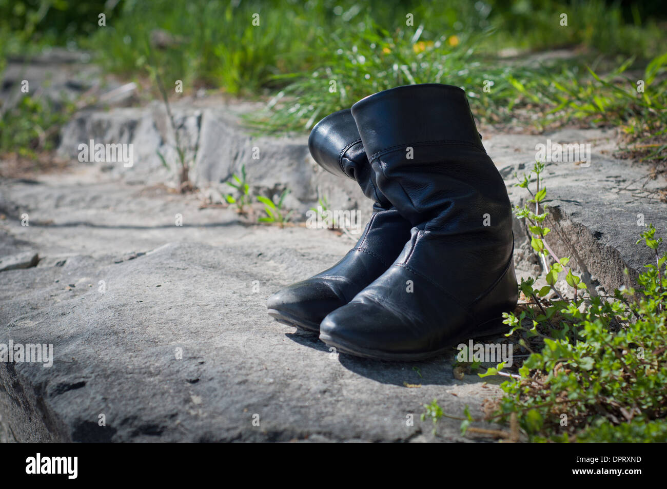 black boots stand among stones and green foliage under bright beams of the sun Stock Photo