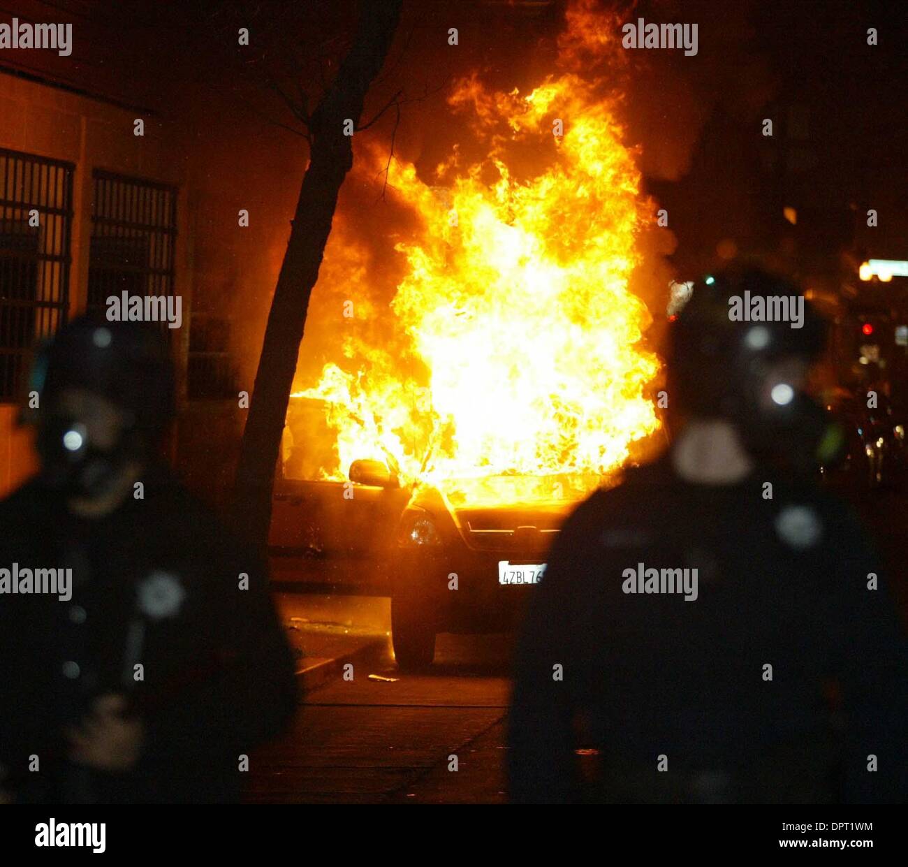A car burns as police push a group of protesters down Fourteenth Street on Wednesday, January 7, 2009, in Oakland, Calif. Demonstrators from a protest against the fatal BART police shooting of Oscar Grant III took to Oakland streets Wednesday night blocking traffic, setting fires and damaging property. Scores of police, including BART police, Oakland Police Department and officers  Stock Photo
