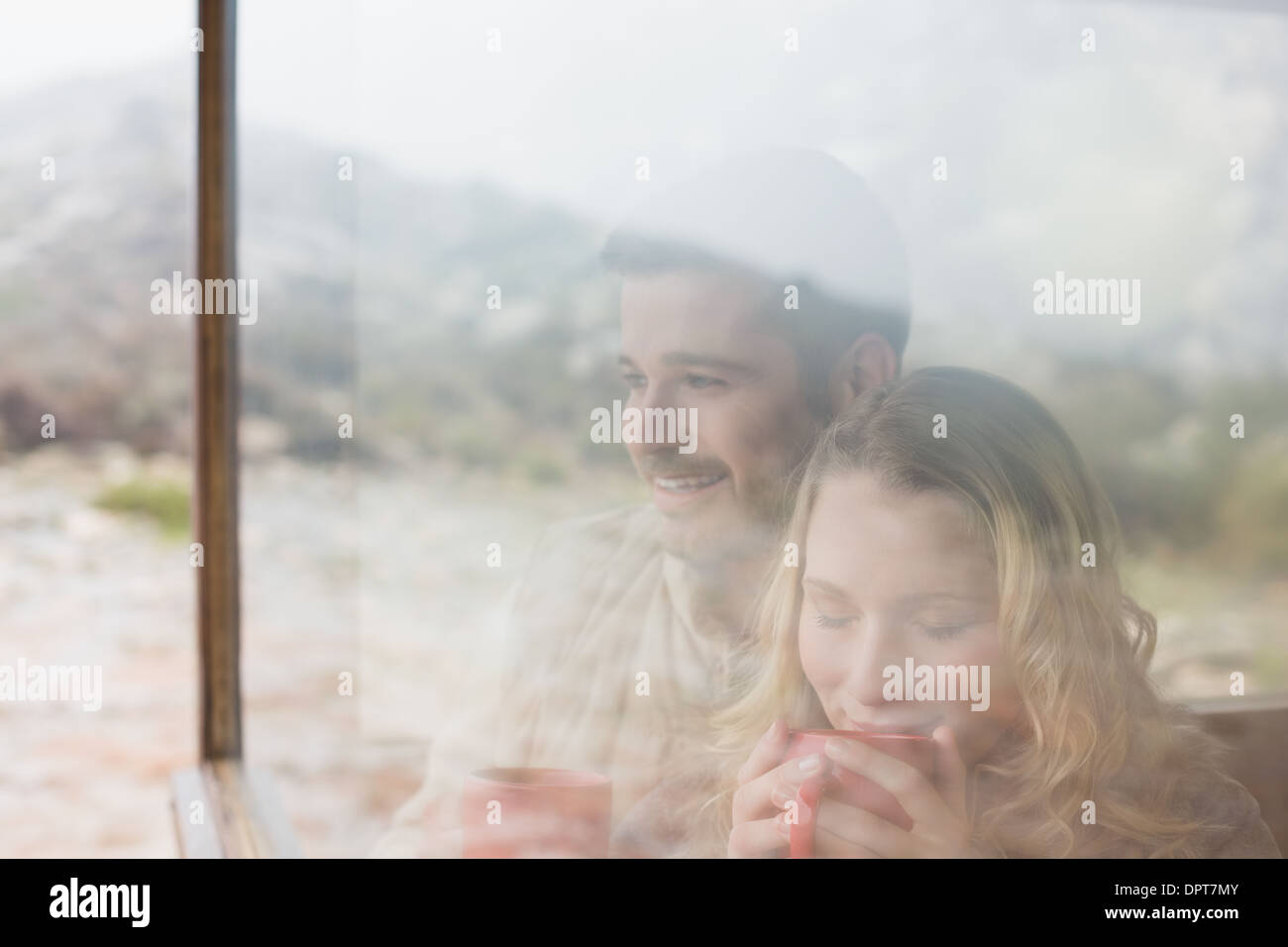 Thoughtful couple with coffee cups seen through cabin window Stock Photo