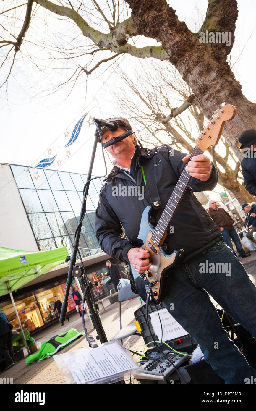 Busker playing electric guitar and mouth organ in town centre. Stock Photo