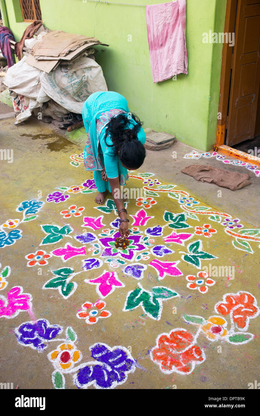 Indian woman lighting an oil lamp on a Rangoli festival coloured powder designs at Sankranti. Andhra Pradesh, India Stock Photo