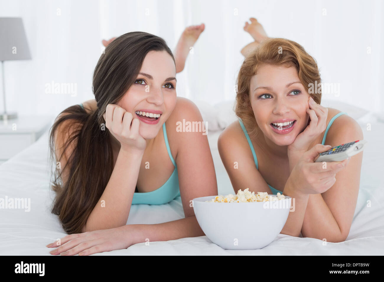 Cheerful friends with remote control and popcorn in bed Stock Photo
