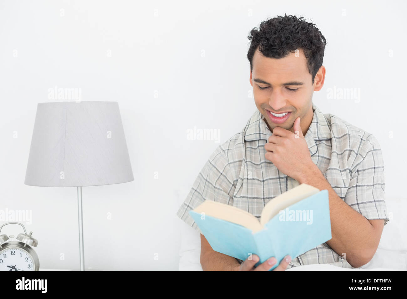 Smiling relaxed man reading book in bed Stock Photo