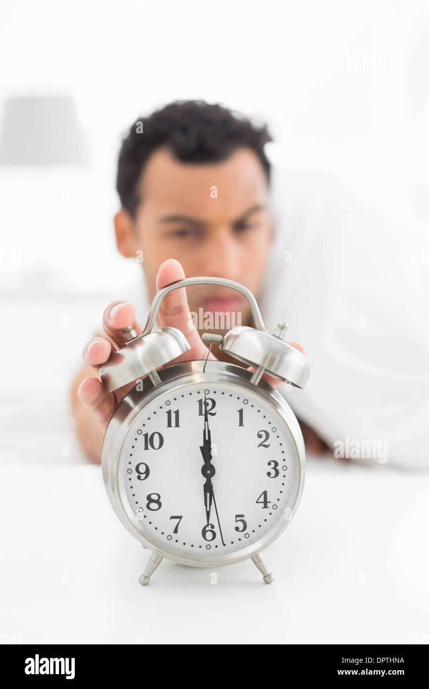 Blurred man in bed extending hand to alarm clock Stock Photo