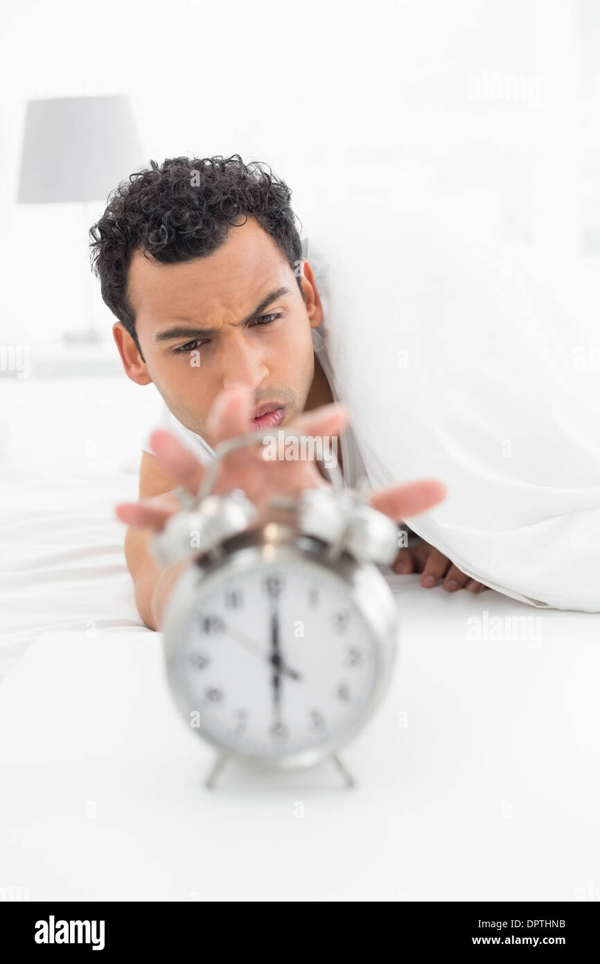 Sleepy man in bed extending hand to alarm clock Stock Photo