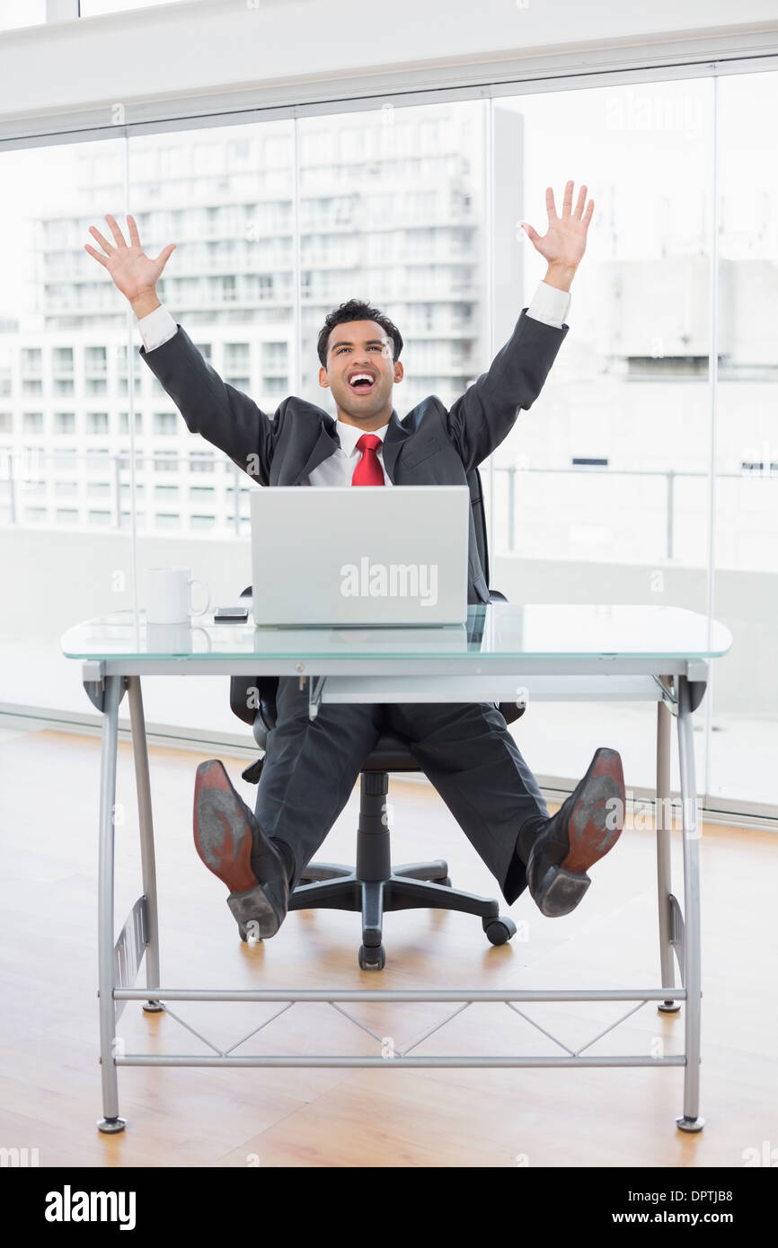 Businessman cheering in front of laptop at office desk Stock Photo