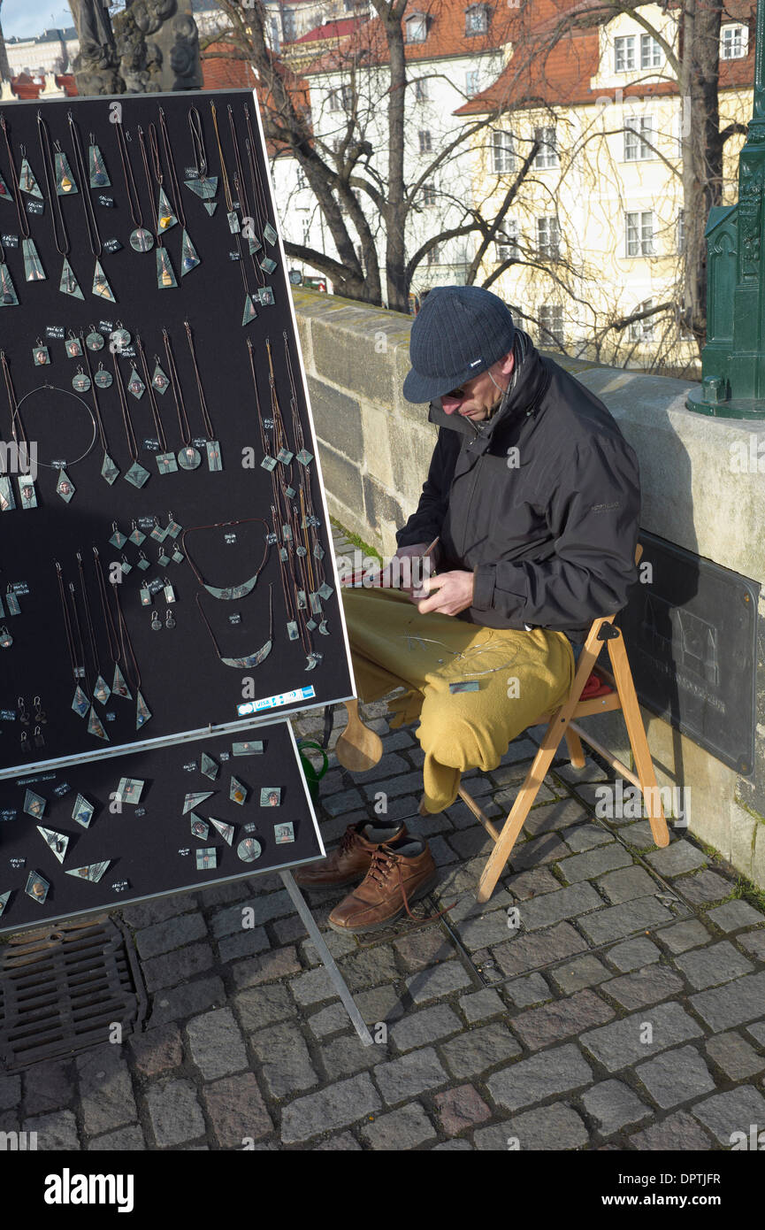 jewelery seller on Charles bridge sits in yoga position working at his craft Stock Photo