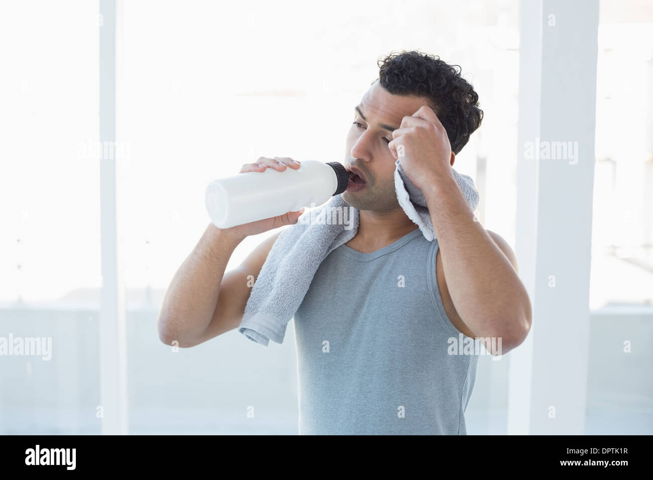 Man drinking water while wiping sweat with towel in fitness studio