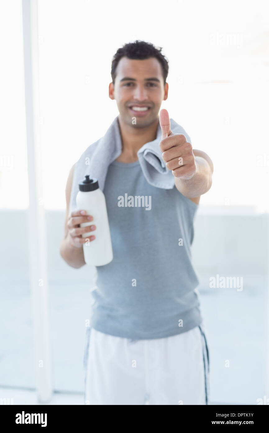 Man with water bottle and towel gesturing thumbs up in fitness studio ...