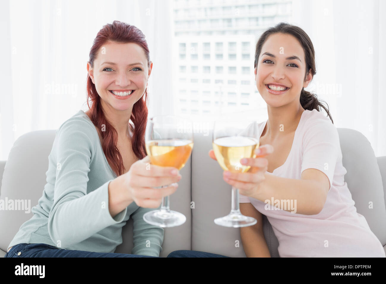Happy female friends holding out wine glasses at home Stock Photo - Alamy