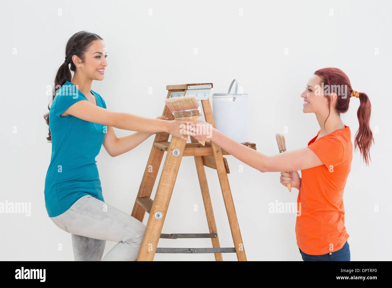Female friends with paint brushes and ladder Stock Photo Alamy