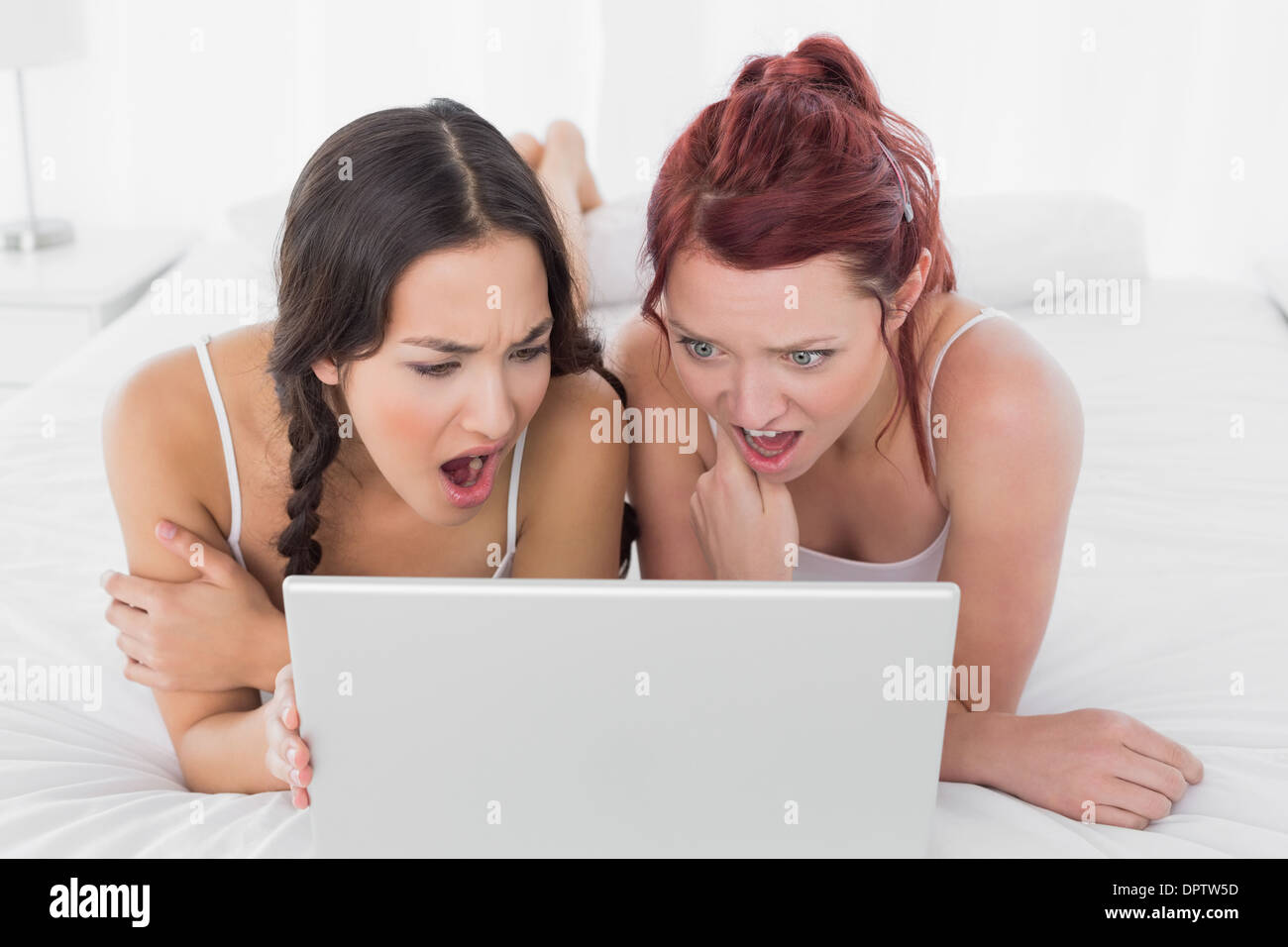 Shocked female friends looking at laptop in bed Stock Photo