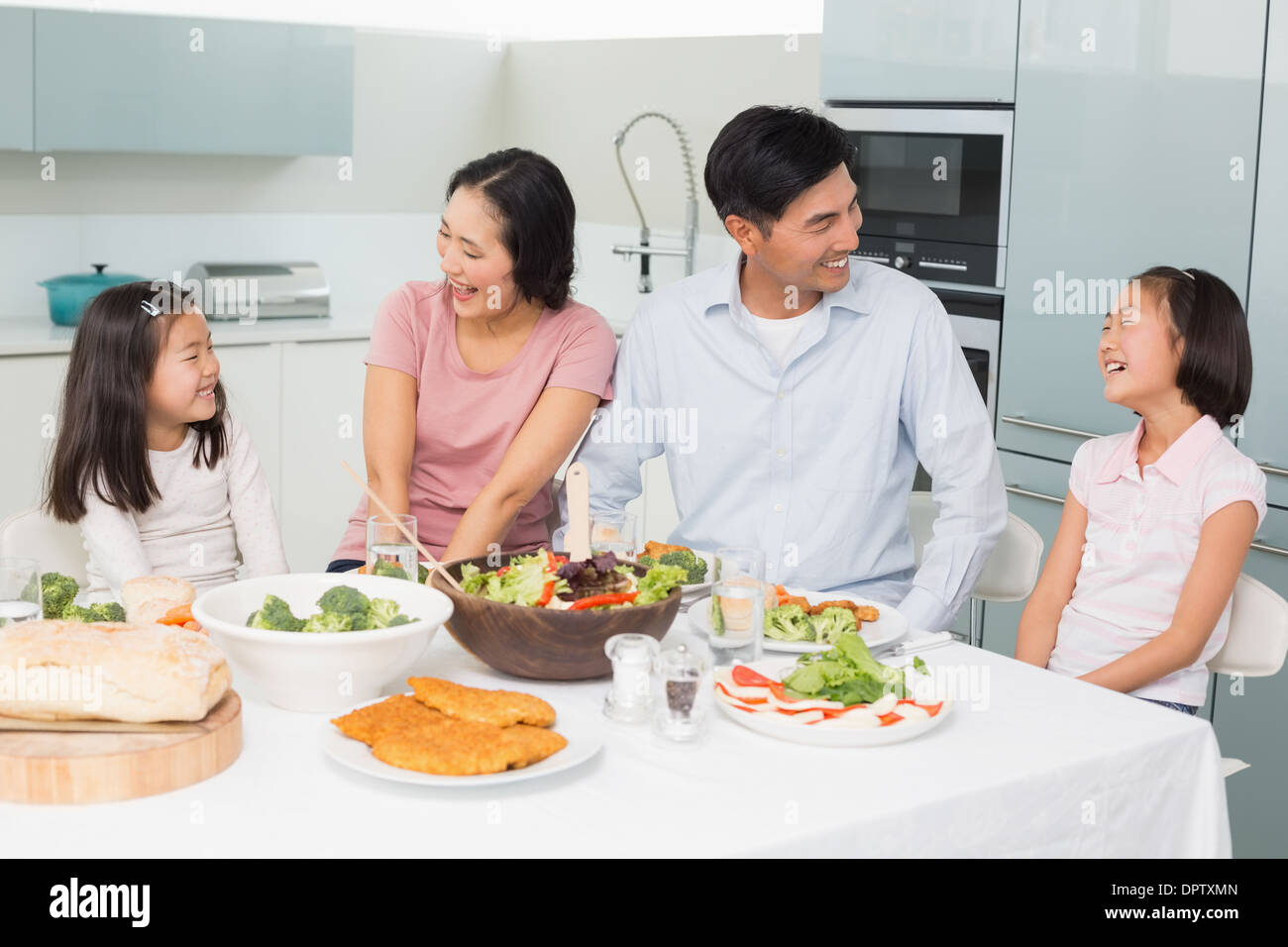 Cheerful family of four enjoying healthy meal in kitchen Stock Photo