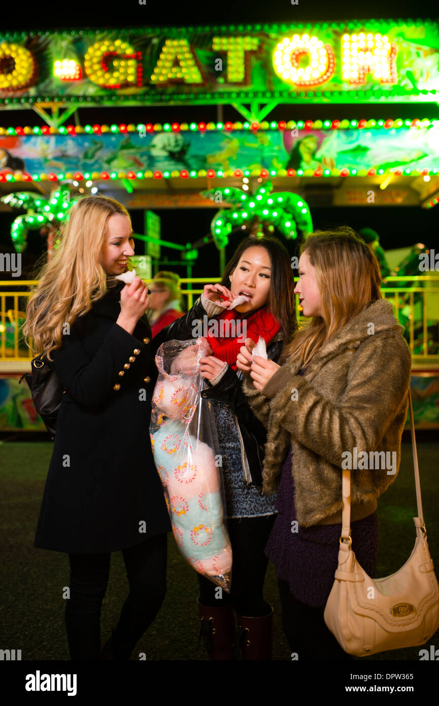 Three young Teenage girls friends young women having fun eating cotton candy candyfloss, at the Aberystwyth November fair fairground amusement arcades, Wales UK Stock Photo