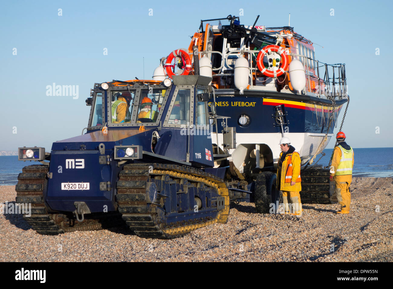 A tractor tows the 'Mersey Class' lifeboat across a shingle beach towards Dungeness RNLI lifeboat station, Kent, England Stock Photo