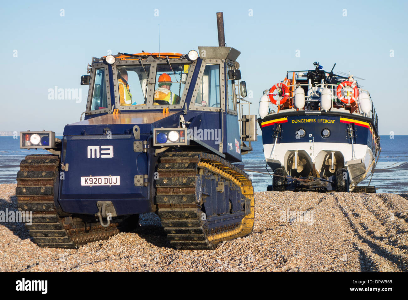 A tractor tows the 'Mersey Class' lifeboat across a shingle beach towards Dungeness RNLI lifeboat station, Kent, England Stock Photo