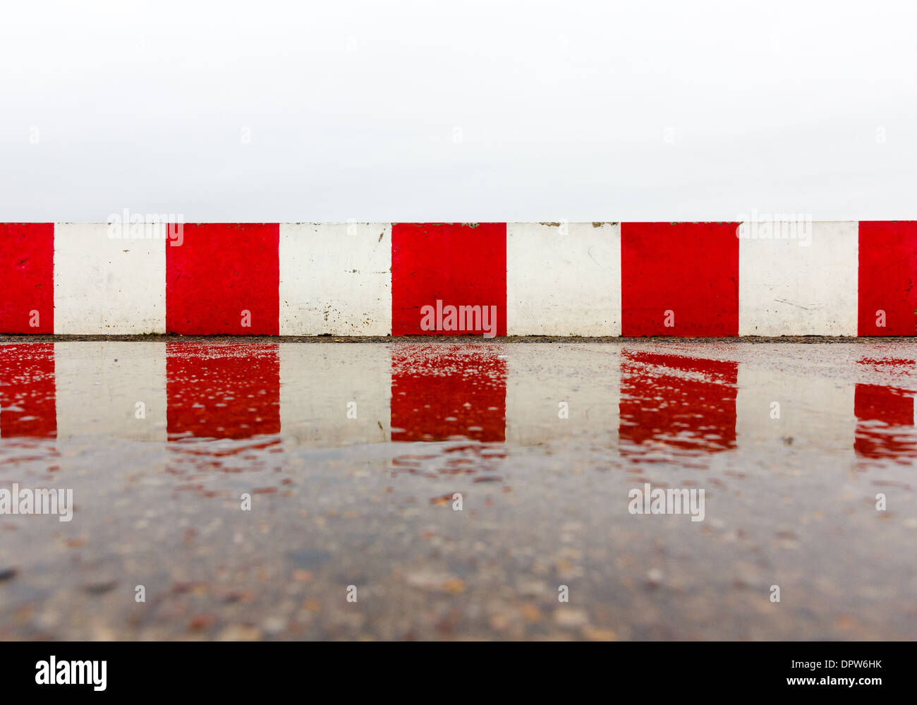 Red white concrete wall on the wet asphalt Stock Photo