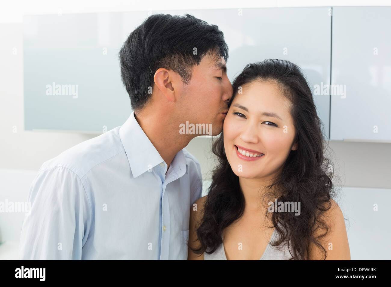 Close-up of a young man kissing woman in kitchen Stock Photo