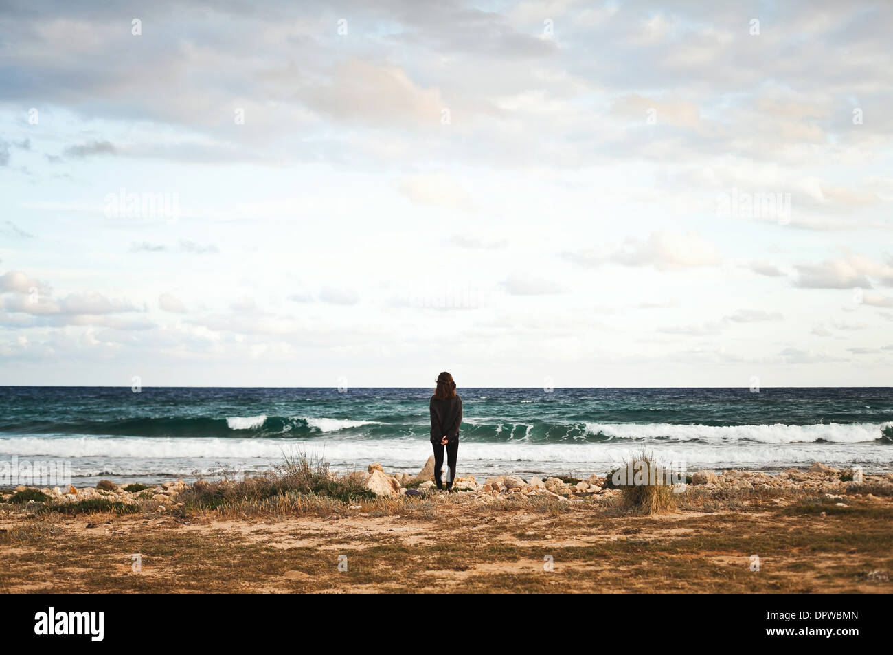 A woman stands on a rocky beach in front of the ocean Stock Photo - Alamy