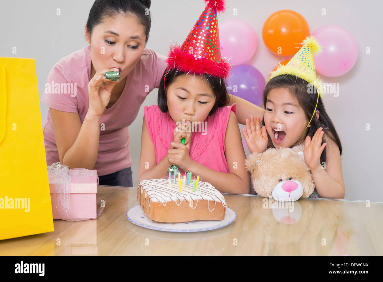 Girls and mother blowing noisemakers at a birthday party Stock Photo