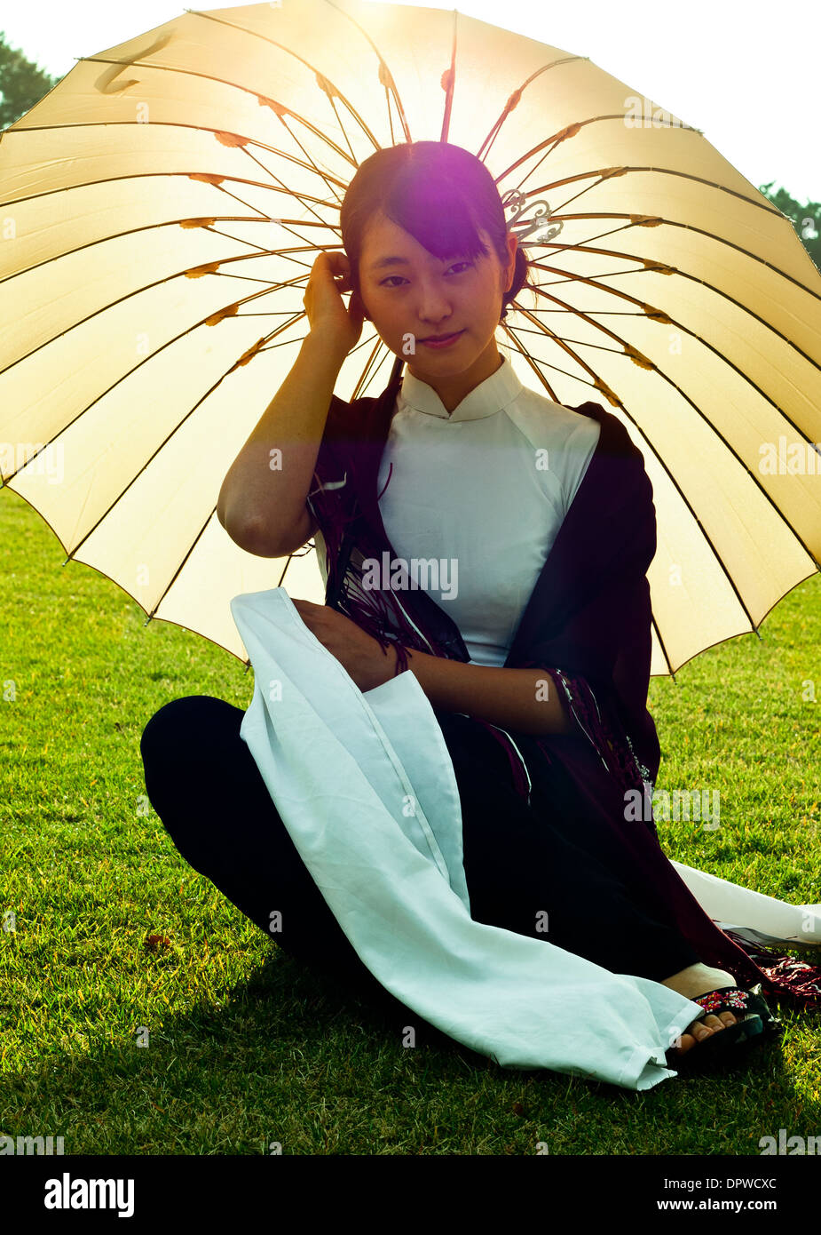 Young Women Glancing at Camera Kneeling in Ao Dai Wear With Umbrella Stock Photo