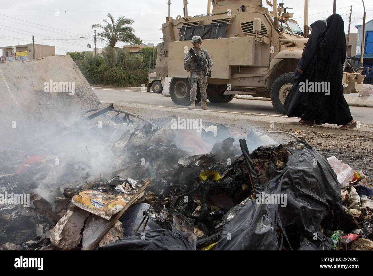 Feb 11, 2009 - Baghdad, Iraq - Sergeant STOWERS of the U.S Army 425 Civil Affairs Battalion stands by an armored vehicle in front of the Ghazalia neighborhood council building as trash burns on the street. Trash disposal in Iraq has been a large problem for the Iraqi government, even with help from the U.S. to train and fund neighborhood trash collection crews.  Trash collecting ha Stock Photo
