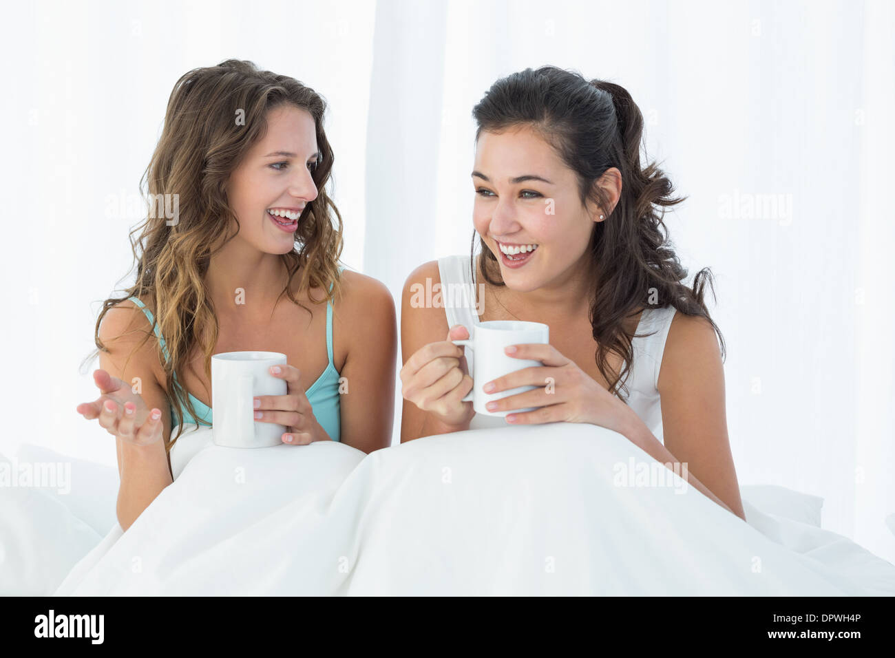 Cheerful friends with coffee cups chatting in bed Stock Photo