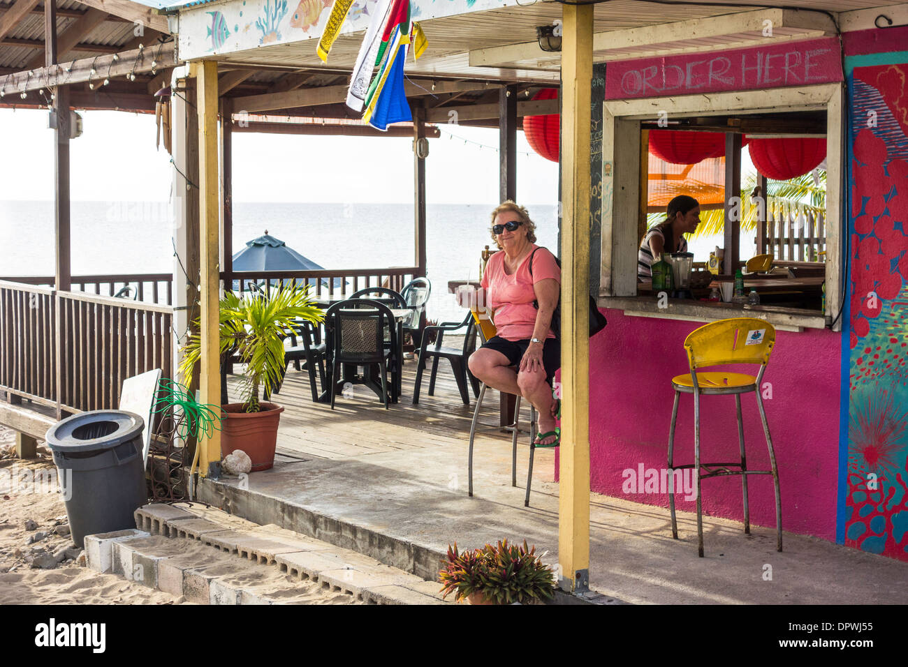 A senior Caucasian woman sits on a stool at a beachside outdoor bar and grill. Frederiksted, St. Croix, U.S. Virgin Islands Stock Photo