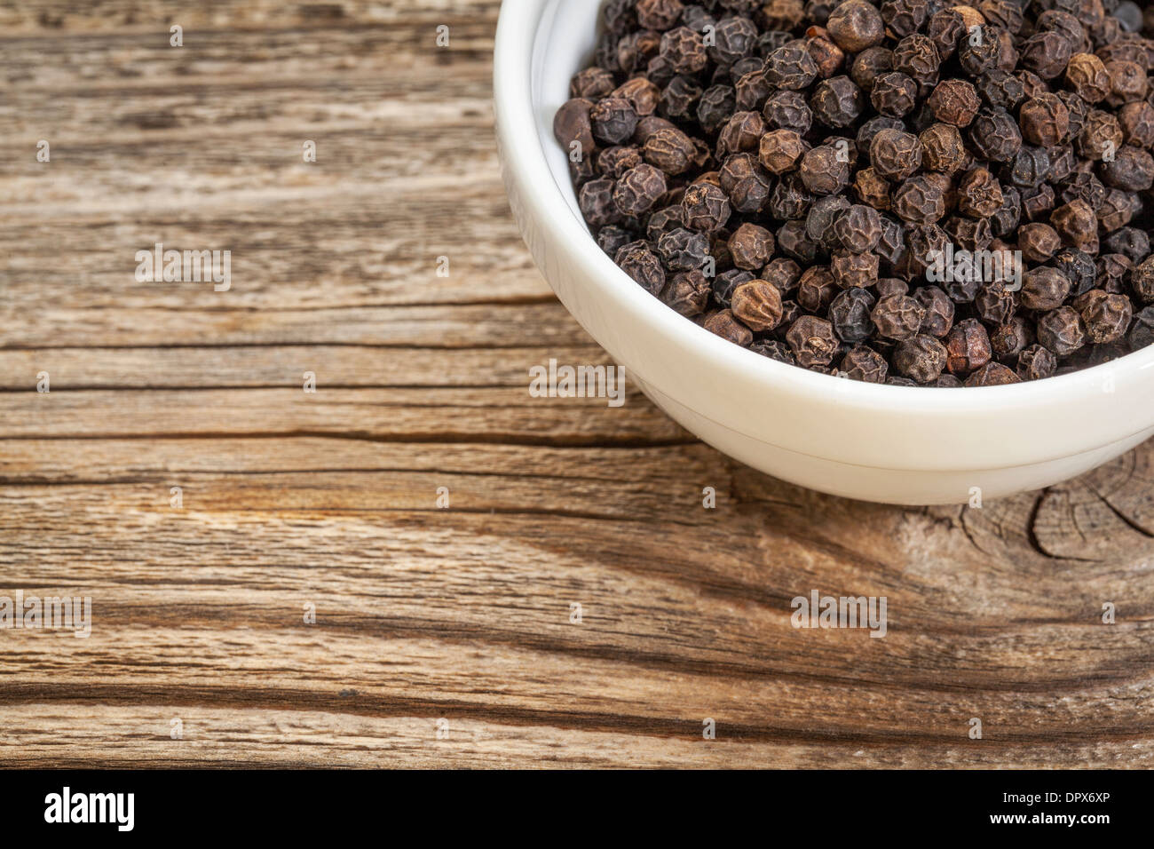 a bowl of black peppercorns against grained wood with copy space Stock Photo