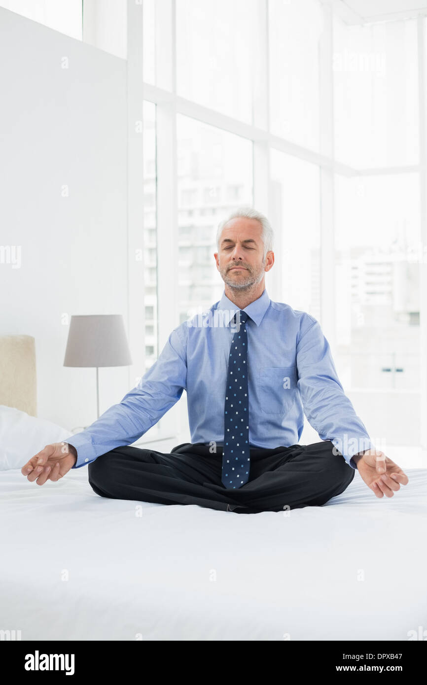 Relaxed mature businessman sitting in lotus posture on bed Stock Photo