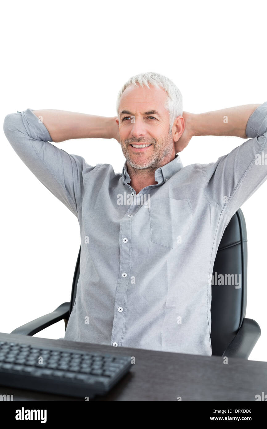 Businessman sitting with hands behind head at desk Stock Photo