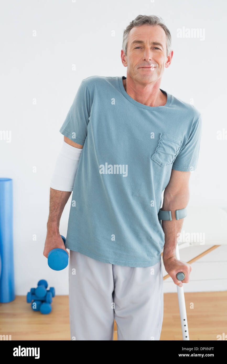 Smiling mature man with crutch and dumbbell Stock Photo