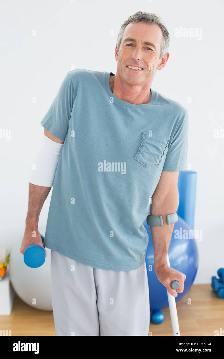 Smiling mature man with crutch and dumbbell Stock Photo