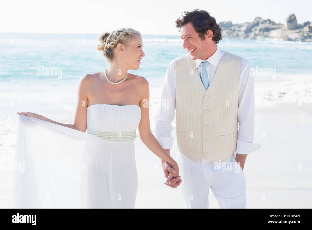 Newlyweds walking hand in hand and smiling at each other Stock Photo