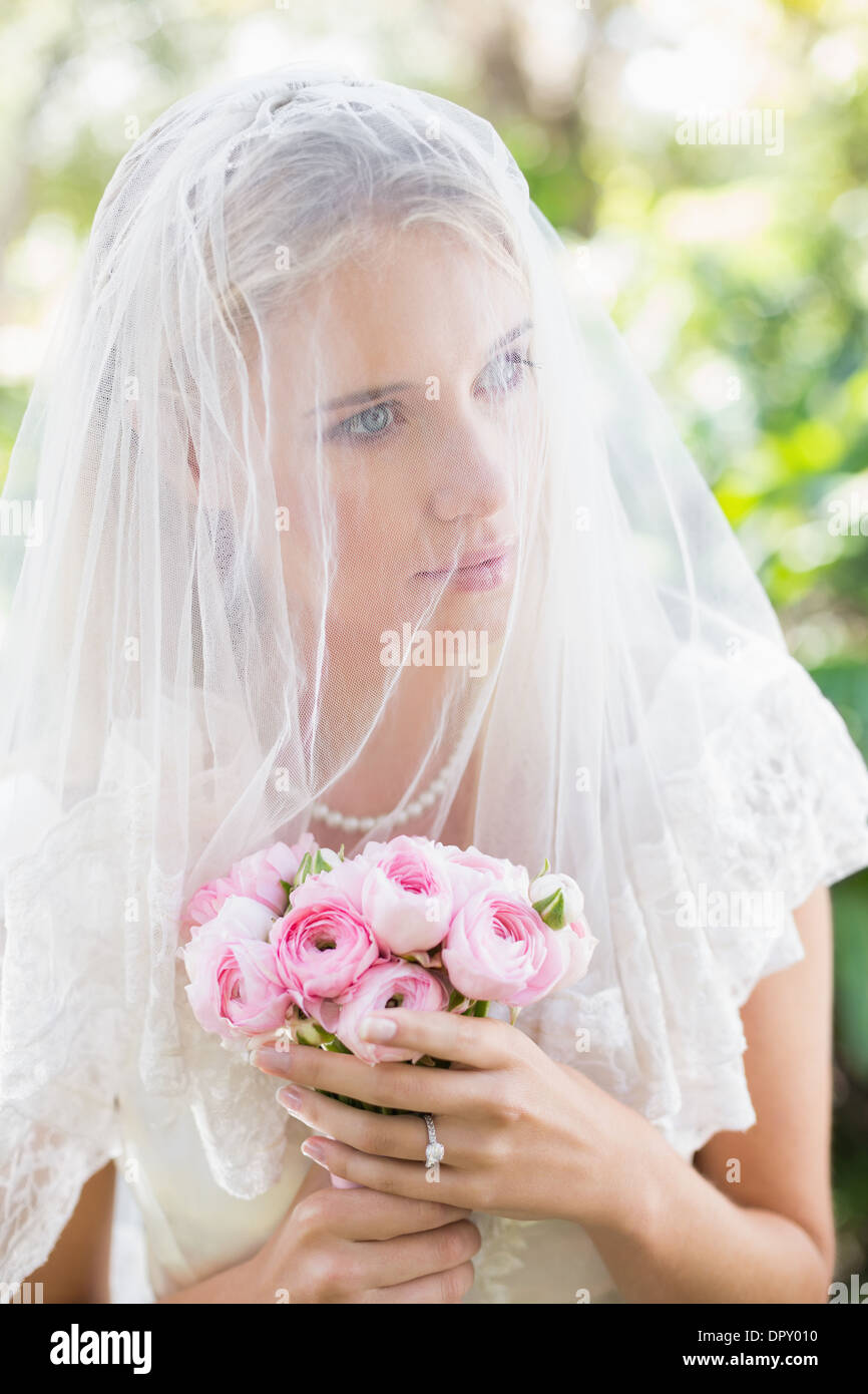 Content bride wearing veil over face holding rose bouquet Stock Photo