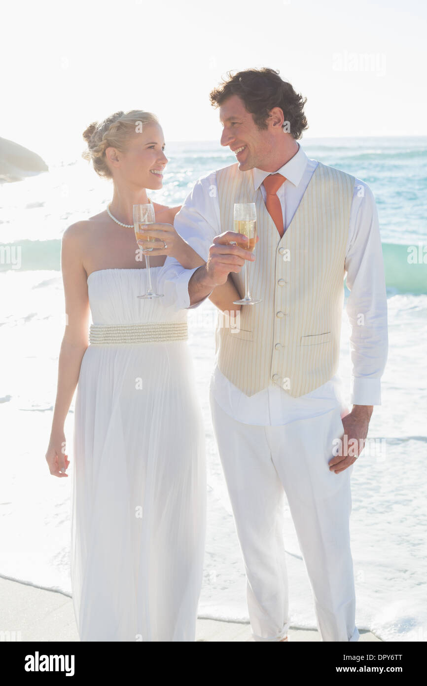 Smiling newlyweds having champagne linking arms Stock Photo
