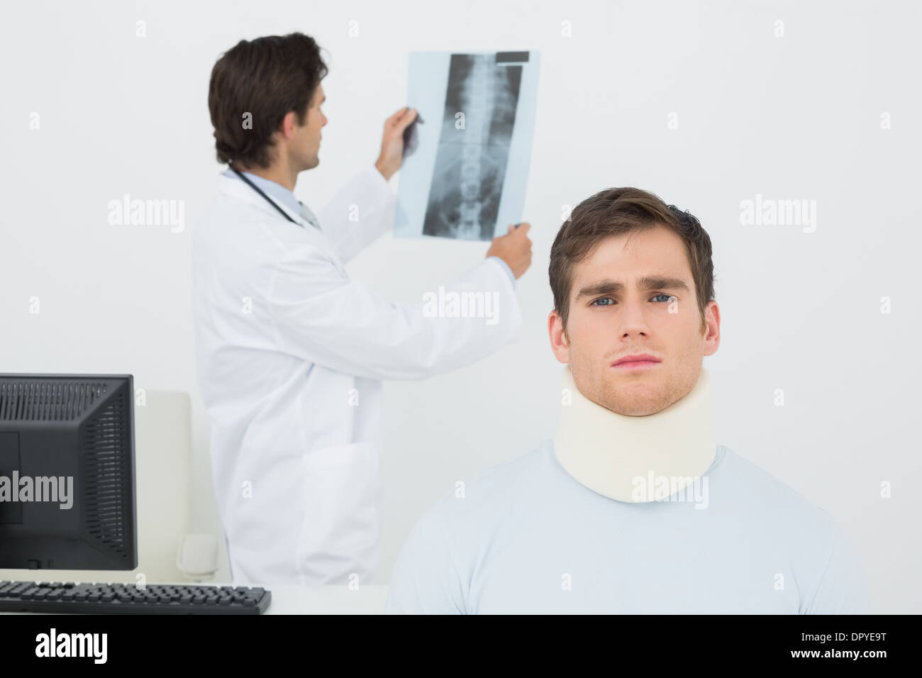 Patient in surgical collar with doctor examining spine x-ray behind Stock Photo
