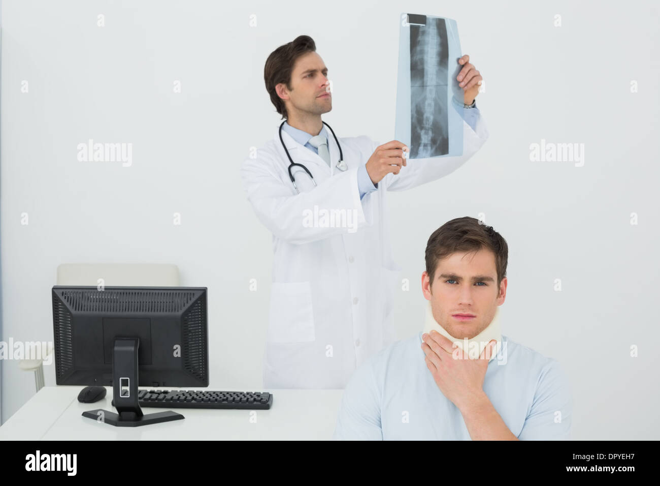 Patient in surgical collar while doctor examining spine x-ray behind Stock Photo