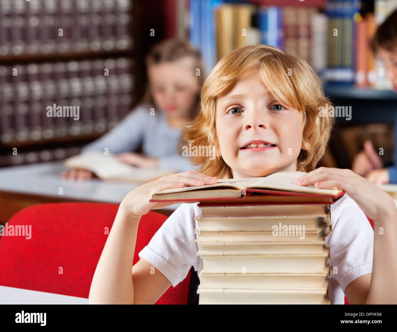 Schoolboy With Stack Of Books Sitting In Library Stock Photo - Alamy