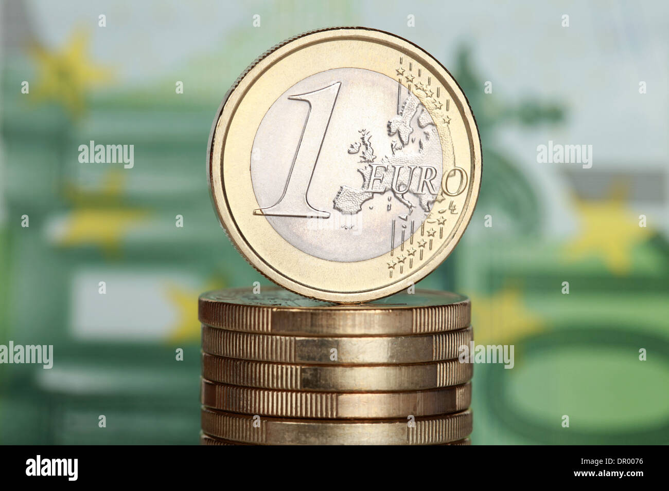 One Euro coin on a stack of Euro coins with a 100 Euro banknote in the background Stock Photo