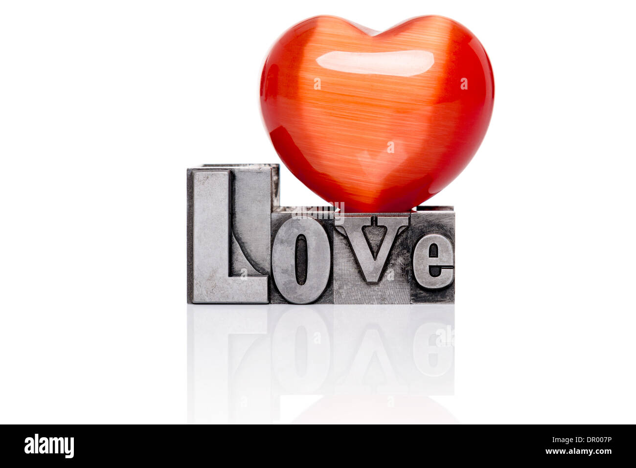 Love in old mixed font metal letterpress blocks with a red gemstone heart on top, isolated on a white background. Stock Photo