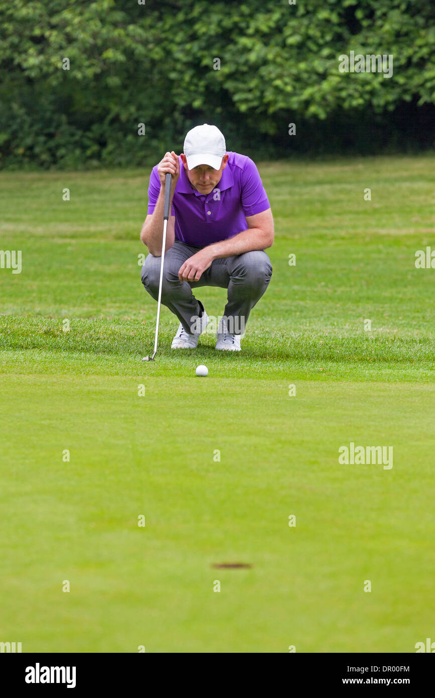 Golfer holding his putter reading the green getting reading to putt as he looks towards the hole. Stock Photo
